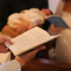 Célébration d'un baptême : un livre ouvert est tenu, un bébé est porté, et des parents écoutent attentivement la bénédiction.