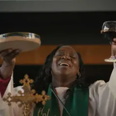 Une femme, peut-être une marraine de substitution, célèbre la communion en levant une coupe de vin et une patène.