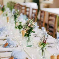Décoration baptême champêtre à faire soi-même : table dressée avec nappes blanches, bouquets de fleurs sauvages, serviettes à carreaux bleus et bois.