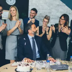Une équipe célèbre le départ à la retraite de son collègue avec un gâteau et des applaudissements. Un texte invitation départ retraite humoristique serait parfait pour cette occasion !
