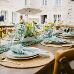 Table dressée pour un thème anniversaire adulte, avec des fleurs bleues et jaunes, des serviettes bleu pâle et des couverts dorés.