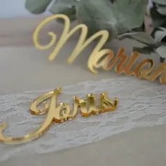 Marque place plexiglas doré "Joris" et "Marion" sur un chemin de table en dentelle, avec des feuilles d'eucalyptus en arrière-plan.