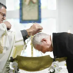 Un prêtre en robe blanche verse de l'eau sur la tête d'un homme penché dans une vasque dorée, un moment sacré qui peut baptiser.