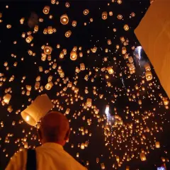 Un homme observe une multitude de lanternes thaïlandaises illuminant le ciel nocturne, créant un spectacle magique.
