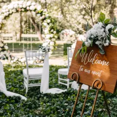 Bienvenue à notre mariage industriel en plein air. Arches florales, chaises blanches et panneau de bienvenue en bois.