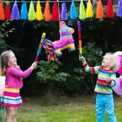 Des enfants joyeux s'amusent à casser une pinata colorée, une scène parfaite pour apprendre comment accrocher une pinata pour une fête.