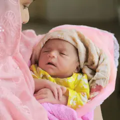 Une mère murmure des prières à l'oreille de son nouveau-né, un moment sacré dans la tradition islamique.