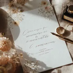 Un faire-part de mariage élégant, orné de fleurs séchées, avec une plume dorée, des alliances et un encrier. Idéal pour une cagnotte mariage.