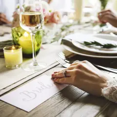 Un verre de champagne et une bougie illuminent une table dressée pour un mariage. La carte "Bride" annonce le cocktail de bienvenue.