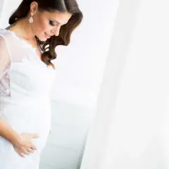 Une future mariée enceinte, vêtue d'une robe blanche, caresse son ventre avec tendresse.