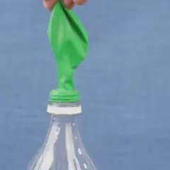 Un ballon vert est posé sur le goulot d'une bouteille en plastique. Une main le tient, prêt à montrer comment gonfler un ballon.