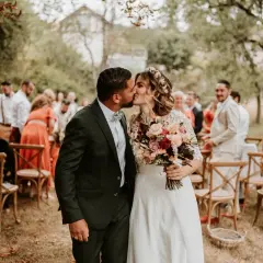 Un couple s'embrasse lors de cérémonies laïques en plein air, entouré d'invités et de chaises en bois.
