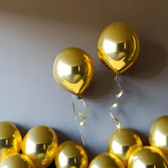 Des ballons dorés brillants flottent près d'un mur. Une astuce pour savoir comment faire tenir des ballons au plafond : utilisez du ruban adhésif double face.