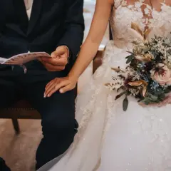 Un couple se tient la main, le marié lit un document, la mariée tient un bouquet. La musique de la sortie de mairie résonne.