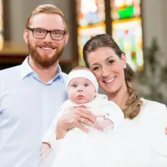 Un couple souriant pose avec leur bébé lors d'un baptême. La question "peut-on être marraine à 11 ans ?" résonne, mais ici, c'est une famille unie.