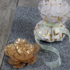 Un sachet dragees a faire soi meme, décoré de motifs dorés, à côté d'une fleur en papier.