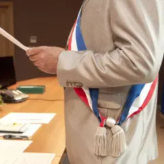 Un maire, portant l'écharpe tricolore, tient un document. Le baptême civil est possible à tout âge.