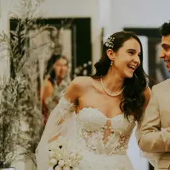 Un couple souriant, une mariée en robe blanche et un marié en costume beige, planifiant leur mariage sur une liste de tâches.