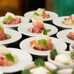 Petits amuse-bouches de jambon cru roulé, melon et garniture verte, prêts pour un dîner assis.