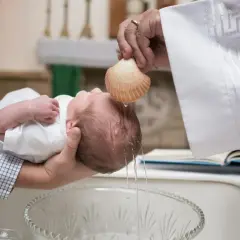 Un bébé est baptisé lors d'une messe. L'eau bénite coule d'une coquille sur sa tête.