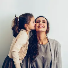 Une petite fille embrasse sa mère sur la joue. Elle pense : "je ne sais pas qui choisir comme marraine", mais l'amour est évident.