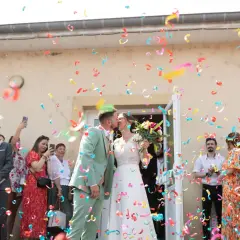 Un couple s'embrasse sous une pluie de confettis colorés, formant une haie d'honneur mariage joyeuse.