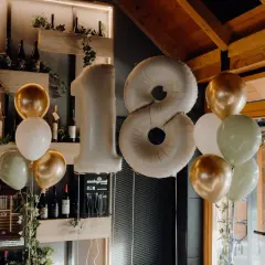 Ballons dorés, blancs et verts flottent près d'un grand ballon chiffre 18, parfait pour une fête d'anniversaire.