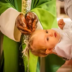 Un bébé est tenu par un parent lors d'un baptême chrétien. L'eau bénite coule des mains du prêtre sur la tête de l'enfant.
