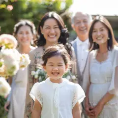 Une famille souriante célèbre un baptême laïque dans un jardin fleuri. La petite fille au premier plan rayonne de joie.