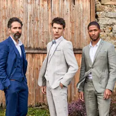 Trois hommes posent devant une porte en bois. Leurs costumes de mariage varient en couleur : bleu marine, gris clair à carreaux et vert sauge.