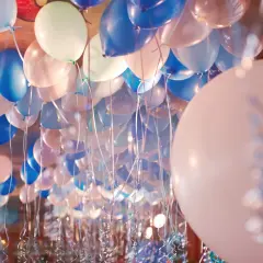 Une multitude de ballons bleus, blancs et roses flottent au plafond, prêts à gonfler avec de l'hélium pour une fête.
