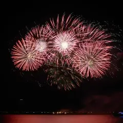 Un spectaculaire feu d'artifice illumine le ciel nocturne au-dessus de l'eau, reflétant ses couleurs vives sur la surface calme.