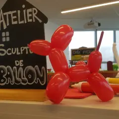 Un chien en sculpture ballon rouge, à côté d'un panneau "Atelier Sculpture de Ballon". Facile à réaliser !