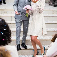 Un couple de mariés, sous une pluie de confettis, s'apprête à lancer la chanson d'ouverture de bal. La mariée tient un bouquet de roses roses.