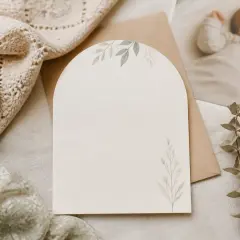 Une carte vierge avec des motifs floraux, prête pour un faire part naissance. Un hochet en bois et une photo de bébé endormi complètent la scène.