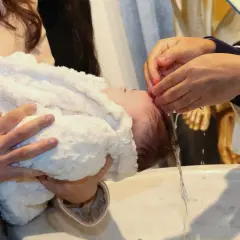 Cérémonie de baptême en hiver. Un bébé est tenu par ses parents, une main verse de l'eau sur sa tête.