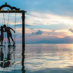 Couple s'embrassant sur des balançoires au coucher du soleil, une parfaite destination lune de miel pas cher.