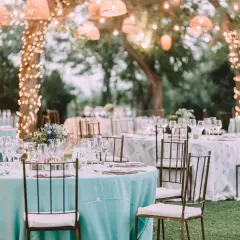 Tables dressées pour un mariage jardin féerique, éclairées par des guirlandes lumineuses dans les arbres.