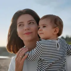 Un poème d'une marraine à sa filleule : une femme tient un bébé sur la plage, le soleil se couche.