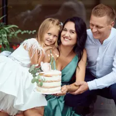 Famille souriante autour d'un gâteau pour un baptême civil ou religieux. La petite fille porte une robe blanche ornée de plumes.