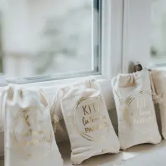 Quatre petits sacs en tissu écru, chacun portant l'inscription dorée "KIT du témoin PARFAIT". Un cadeau témoin mariage personnalisé, prêt à être offert.
