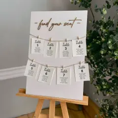 Un panneau "Trouvez votre siège" avec des cartes de table numérotées, chacune avec des noms d'invités. Un marque place vierge est visible sur la carte de la table 8.