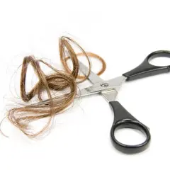Ciseaux coupant une mèche de cheveux de bébé sur fond blanc.