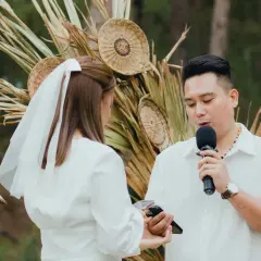 Un homme prononce un discours de mariage devant une femme voilée, micro en main, lors d'une cérémonie en plein air.