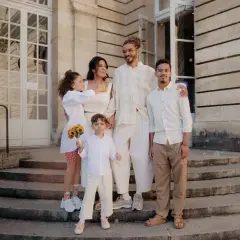 Famille réunie devant un bâtiment, le couple marié entouré de leurs enfants. La plus jeune porte un bouquet de tournesols, un vrai témoin mariage.