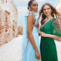 Deux femmes élégantes posent devant des ruines. L'une porte une robe bleu ciel plissée, l'autre une robe verte. Idées pour comment s'habiller pour un mariage.