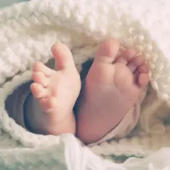 Les petits pieds d'un bébé, enveloppés dans une couverture douce, symbolisant le rôle de parrain/marraine après le décès des parents.