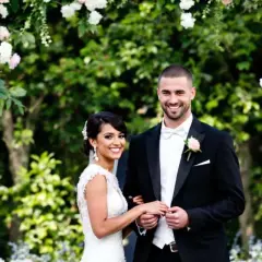 Un couple souriant, paré pour leur cérémonie d'engagement mariage, sous une arche fleurie.