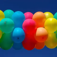 Un amas de ballons colorés flottant dans un ciel bleu. Combien de temps tient un ballon gonflé à l'air ? Cela dépend de sa taille et du matériau.