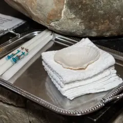 Sur un plateau argenté, des bougies ornées de colombes et d'une croix bleue, symboles de la démarche baptême, attendent près d'une coquille et de serviettes blanches.